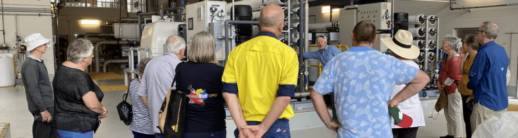 Group of tour participant watching and listening to a tour guide demonstrating the facility inside a recycled water plant