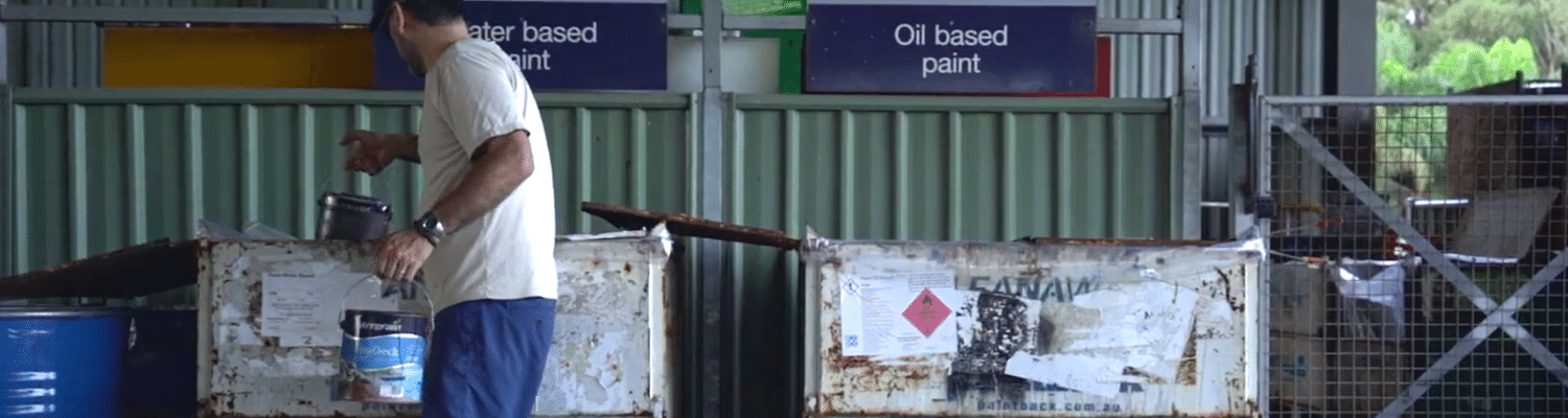 Adult male placing old tin of paint into a community recycling centre bin labelled water based paint