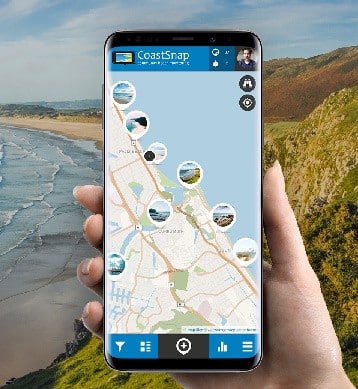 A hand holding a phone with a screenshot of the CoastSnap app. Longshot of beach in background.